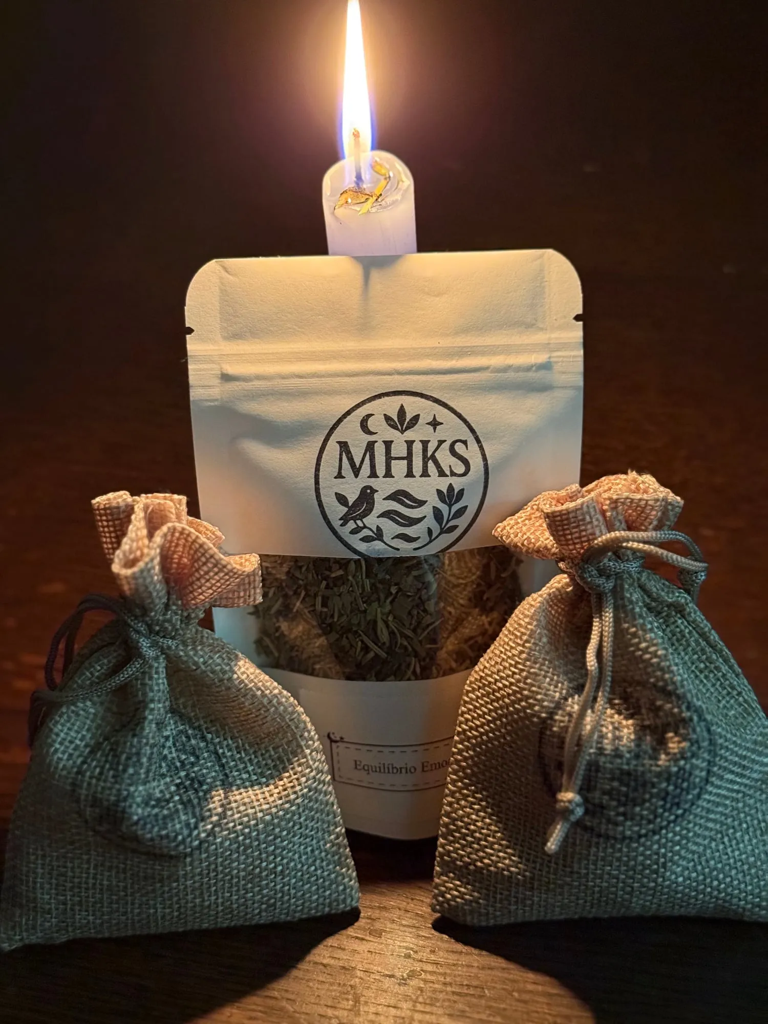 Saqueta de ervas Mundo Holístico com uma vela acesa e dois sachês de juta